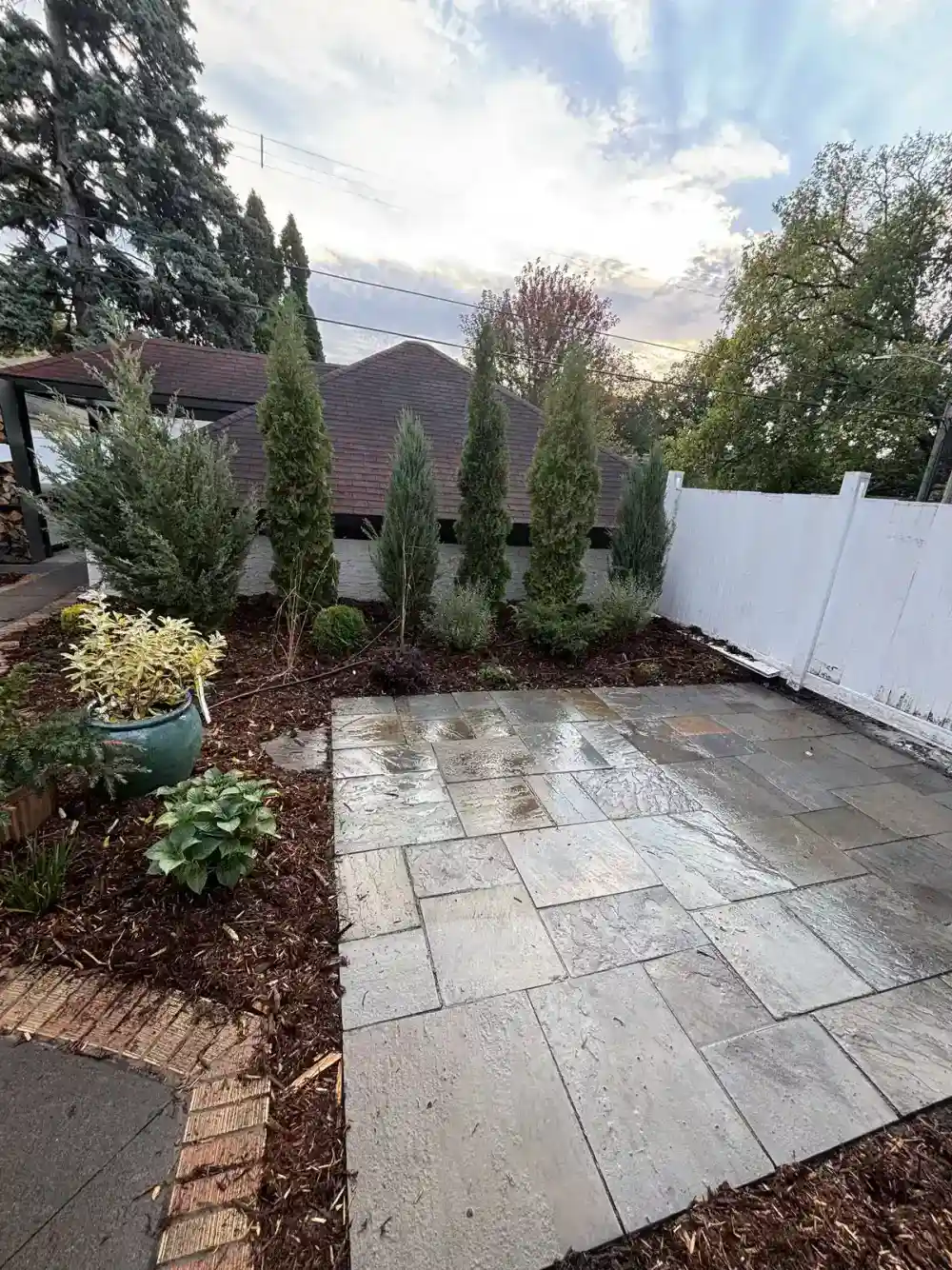Full bluestone patio installation with brick border, hosta plantings, and arborvitae privacy wall in Edina, MN