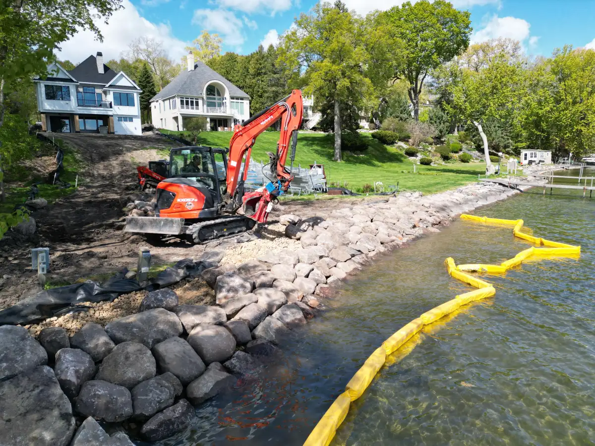 Excavator placing fieldstone boulders for rip rap shoreline stabilization on Lake Minnetonka in Orono