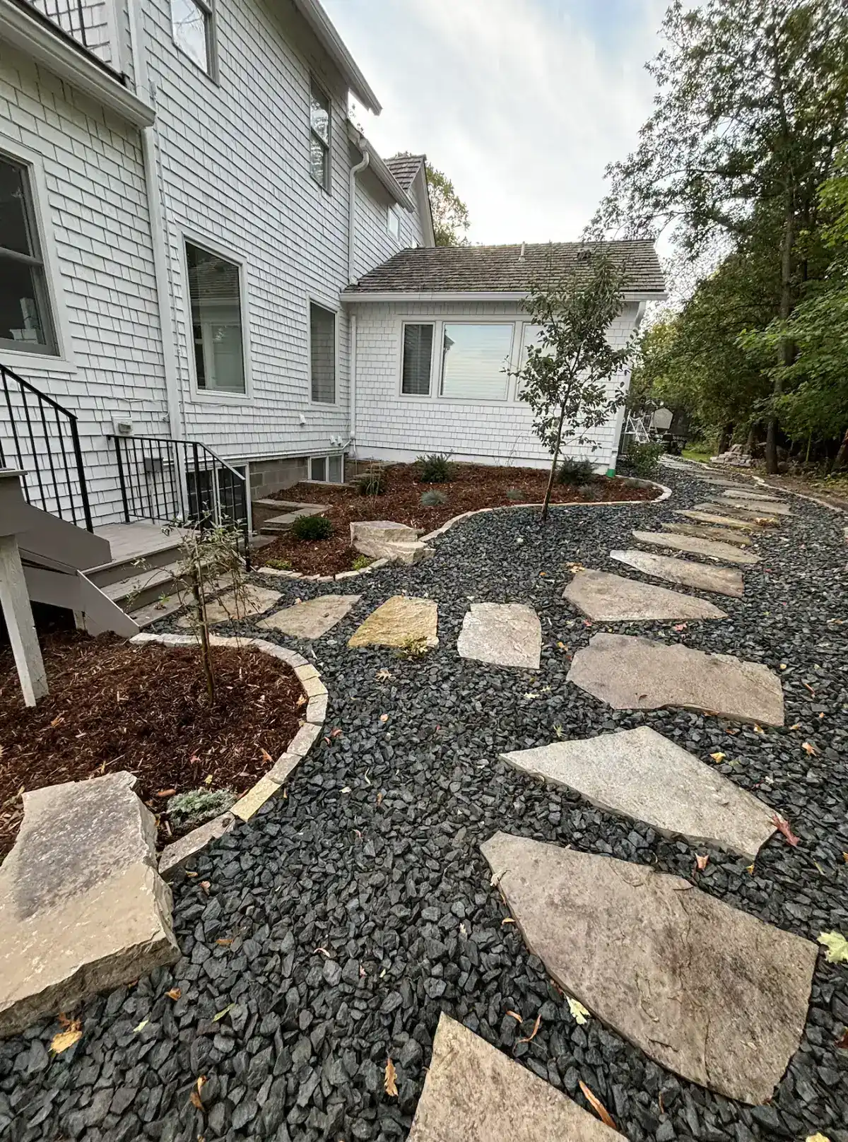 Natural stone stepping path curving past house with outcropping boulders and cedar mulch beds in Orono, MN