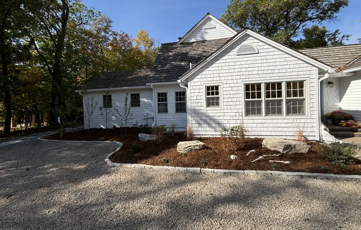 Front of home with completed landscaping — outcropping boulders, cedar mulch beds, new trees, and gravel driveway in Orono, MN